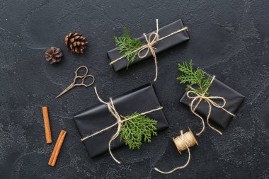 Noel hediye kutularında kozalaklı dallar ve siyah arka planda tarçın var.