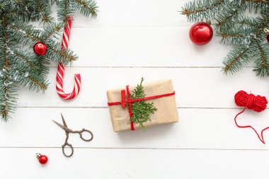 Beyaz ahşap arka planda Noel ağacı dalları, toplar ve şeker kamışları olan hediye kutusu.