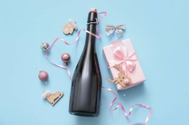 Noel süslemeleri ve mavi arka planda hediye kutusu olan bir şişe şampanya.