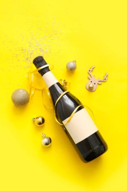Sarı arka planda Noel süslemeleri olan bir şişe şampanya.
