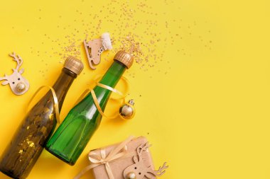 Noel süslemeleri ve sarı arka planda hediye kutusu olan şampanya şişeleri.