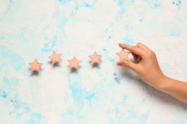 Female hand with five stars rating on light blue grunge background. Customer experience concept
