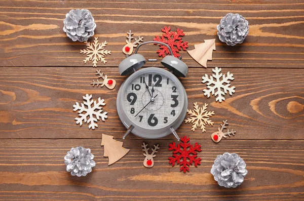 Christmas composition with alarm clock, silver pine cones and snowflakes on brown wooden background