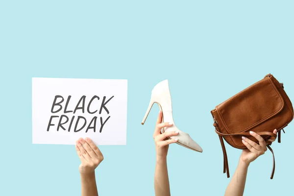 Female hands holding poster with text BLACK FRIDAY and women accessories on blue background