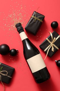 Bir şişe şampanya ve kırmızı arka planda hediye kutuları.