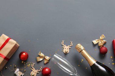 Cam kaplı bir şişe şampanya, Noel süslemeleri ve gri arka planda hediye kutusu.