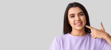 Genç bir kadın gülüşünü açık arkaplanda işaret ediyor, mesaj için yeri var.