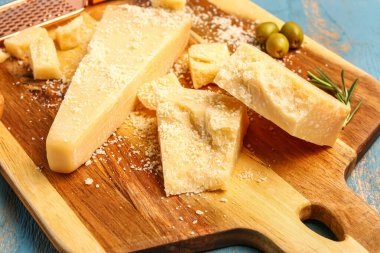 Mavi ahşap arka planda lezzetli parmesan peyniri parçaları olan tahta, yakın plan.