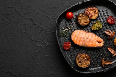 Lezzetli ızgara somon bifteği ve siyah arka planda sebze kızartma tavası