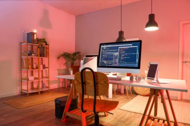 Karanlık ofisin içinde cihazları olan programcının çalışma yeri