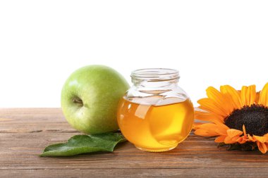 Tatlı bal kavanozu, yeşil elma ve ayçiçeği ahşap masada beyaz arka planda