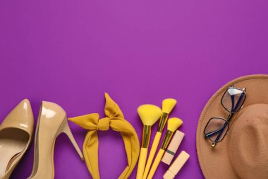 Kadın aksesuarları, kozmetik ürünleri ve mor arka planda yüksek topuklu ayakkabılar.