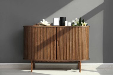 Boş cenaze iskeleti, yanan mumlar, morg vazosu ve ahşap dolapta gri duvara karşı zambak çiçekleri.