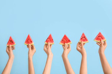 Mavi arka planda olgun karpuz dilimleriyle kadın elleri
