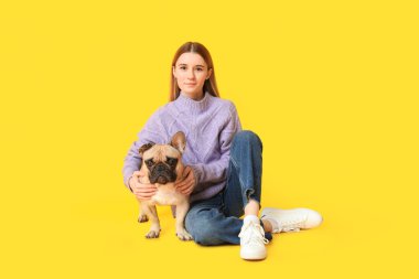 Sarı arka planda oturan sevimli köpekli güzel genç bir kadın.