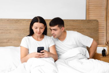 Cep telefonu ve yatak odasında erkek arkadaşı olan genç bir kadın.