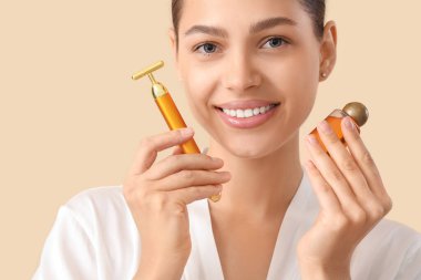 Yüz masajı aleti ve bej arka planda yağı olan güzel bir genç kadın, yakın plan.