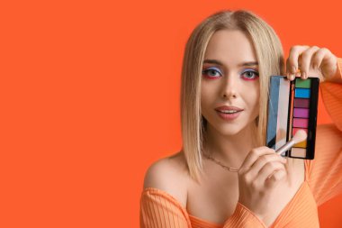 Turuncu arka planda renkli göz falı fırçası ve paleti olan güzel genç bir kadın.