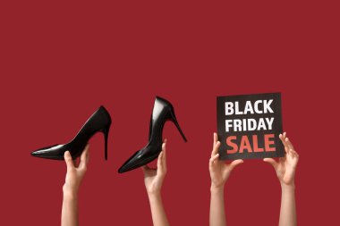 Siyah Cuma satışı ve kırmızı zemin üzerinde şık ayakkabılar olan afiş tutan kadın elleri
