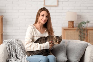 Evdeki kanepede oturan sevimli tekir kediyi tutan genç ve güzel bir kadın.