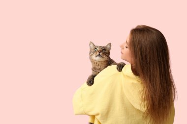 Pembe arka planda sevimli tekir kedisi olan güzel genç bir kadın.