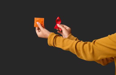 Siyah arka planda kırmızı kurdeleli ve prezervatifli bir kadın eli. Dünya AIDS Günü konsepti