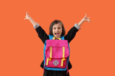 Turuncu arka planda sırt çantası olan mutlu küçük okul kızı.