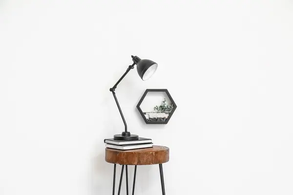 Desk lamp on small wooden table and florarium near white wall