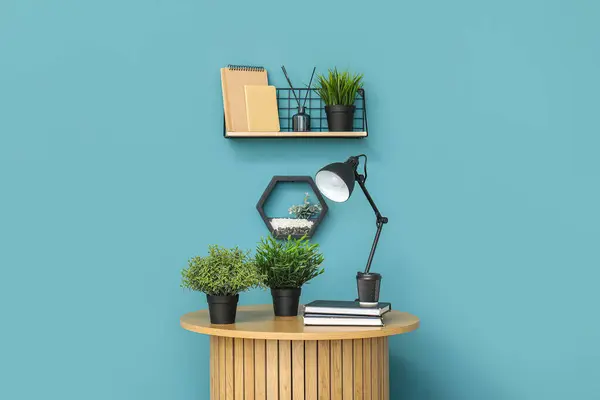 Desk lamp and houseplants on small wooden table near blue wall