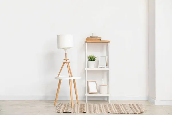 Lamp on small table and shelving unit with decor near white wall