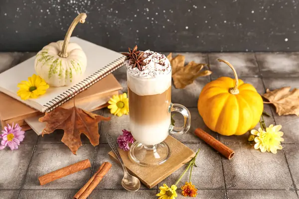 Glass cup of tasty pumpkin latte with star anise and cinnamon on grey tile table