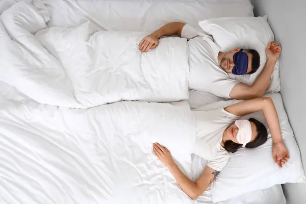 Young couple sleeping with masks in bedroom, top view