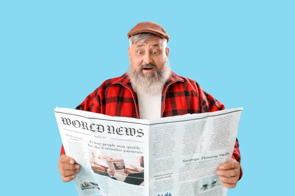 Mature shocked man with newspaper on blue background