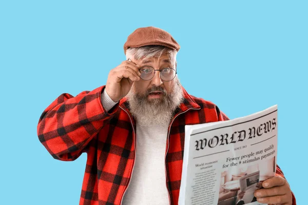 Mature shocked man with newspaper on blue background