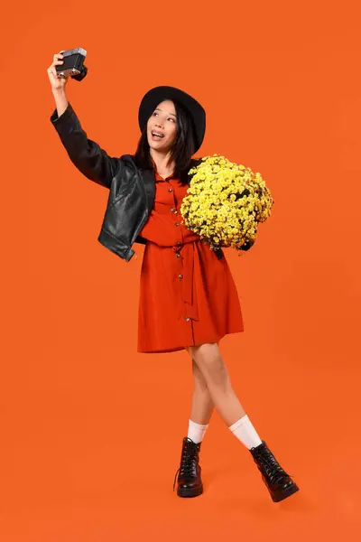 オレンジ色の背景に写真カメラと菊の花を持つ若いアジアの女性 — ストック写真