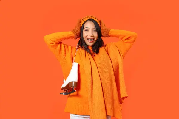 オレンジ色の背景にアイススケートと冬の服の若いアジアの女性 — ストック写真