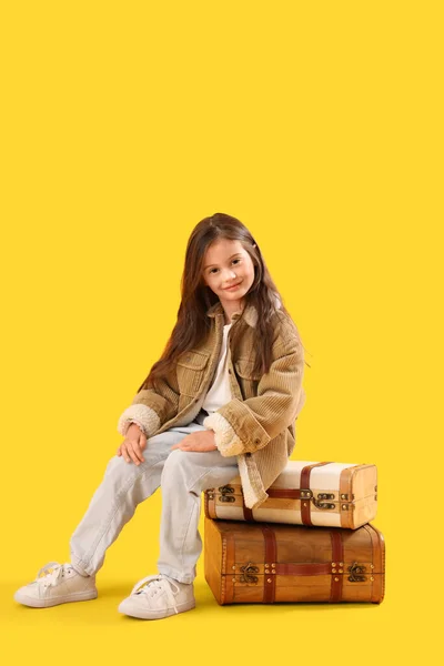 黄色の背景にスーツケースに座っている冬の服の小さな女の子 — ストック写真