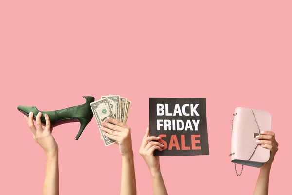 Female hands holding poster with text BLACK FRIDAY SALE, women accessories and money on pink background