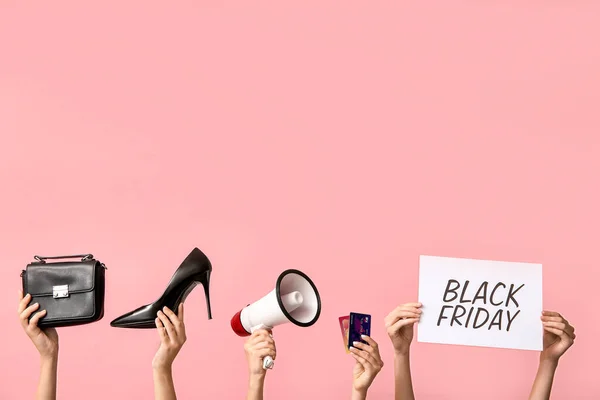 Female hands holding poster with text BLACK FRIDAY, women accessories, megaphone and credit cards on pink background