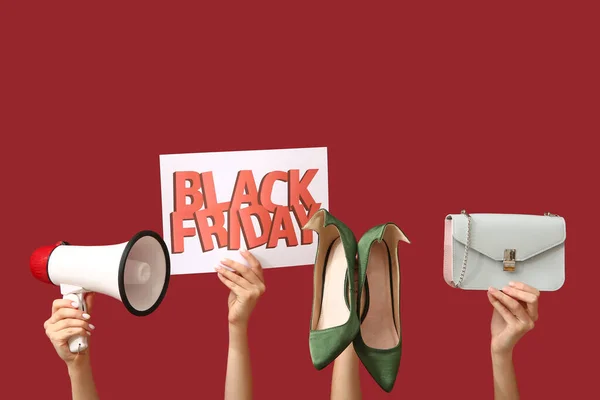 Female hands holding poster with text BLACK FRIDAY, megaphone and women accessories on red background