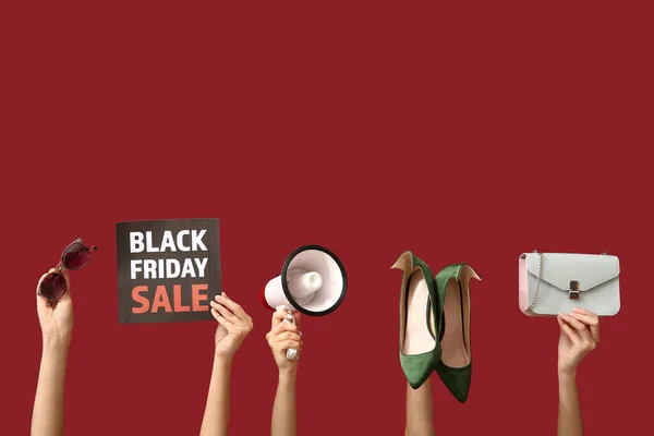 Female hands holding poster with text BLACK FRIDAY SALE, megaphone and women accessories on red background