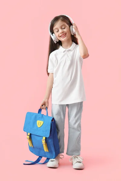 ピンクの背景にバックパックとヘッドフォンでかわいい小さな女子高生 — ストック写真