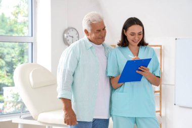 Rehabilitasyon merkezindeki yaşlı hastaya panoda bir şey gösteren kadın doktor.