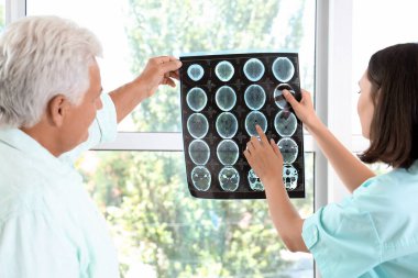 Kadın doktor muayenehanedeki yaşlı hastaya röntgen taraması gösteriyor.