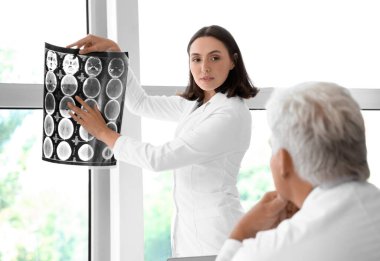 Doktorlar pencerenin yanındaki muayenehanede röntgen taramasını inceliyor.