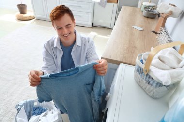 Genç adam çamaşır makinesinden temiz çamaşır alıyor.