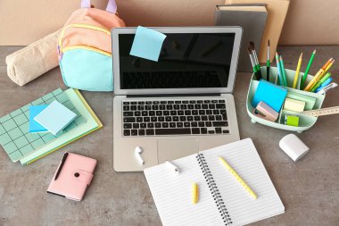 Modern dizüstü bilgisayar, kulaklık ve masasında farklı okul kırtasiyesi olan bir tutucu.