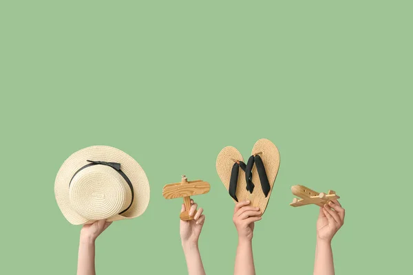 Female hands with hat, wooden airplanes and flip flops on green background. Travel concept