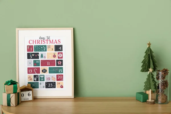 Christmas calendar with presents and decor on shelf near green wall