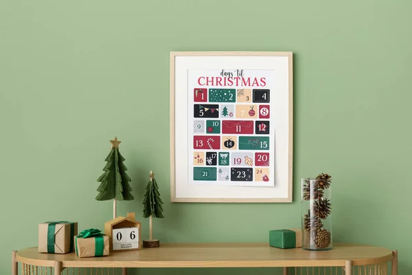 Shelf with presents, decor and Christmas calendar on green wall